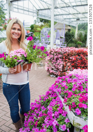 Woman holding two terra cotta pots with pink petunias, standing under greenhouse canopy, copy space Woman holding two terra cotta pots with pink petunias, standing under greenhouse canopy, copy space 135307526