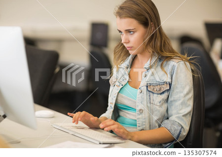 Woman typing on external keyboard at computer lab workstation wearing denim jacket and striped top Woman typing on external keyboard at computer lab workstation wearing denim jacket and striped top 135307574