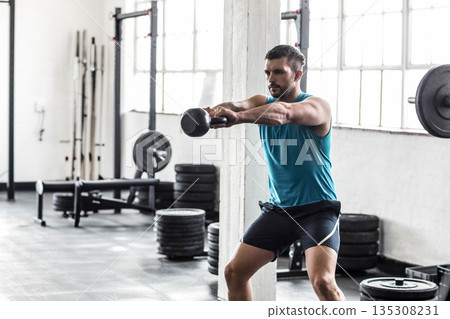 Man wearing sportswear holding kettlebell in squat stance at gym with weight plates, copy space Man wearing sportswear holding kettlebell in squat stance at gym with weight plates, copy space 135308231