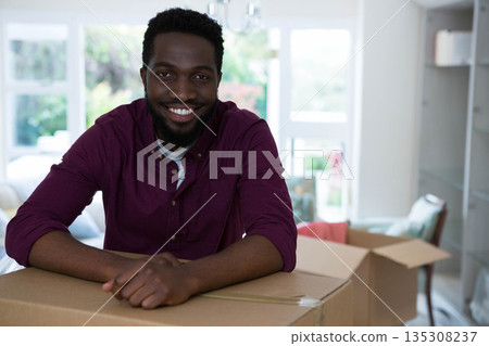 African American man leaning on cardboard box under chandelier at home surrounded by moving boxes African American man leaning on cardboard box under chandelier at home surrounded by moving boxes 135308237