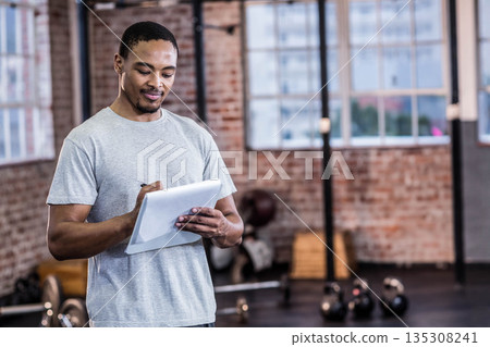 African American man holding tablet and stylus while tracking kettlebell workouts in brick gym 135308241