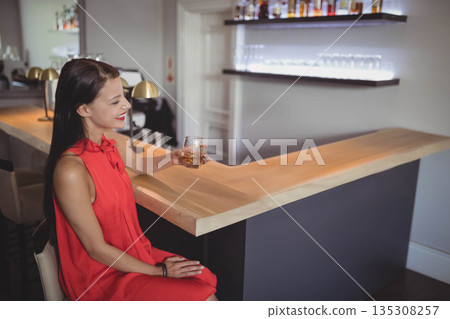 Native American woman sipping drink from short glass at bar with backlit liquor bottles, copy space Native American woman sipping drink from short glass at bar with backlit liquor bottles, copy space 135308257