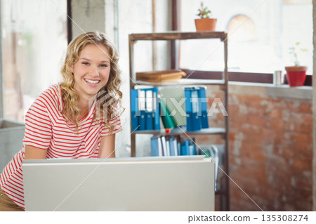 Female adolescent leaning behind monitor in brickwalled office with binders and plant, copy space Female adolescent leaning behind monitor in brickwalled office with binders and plant, copy space 135308274
