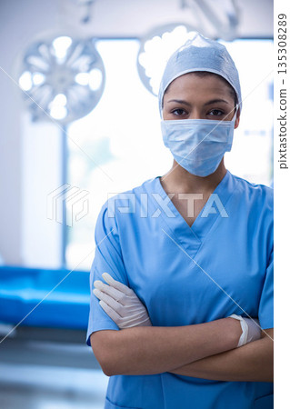 African American woman surgeon wearing scrubs standing under lights, arms crossed in operating room African American woman surgeon wearing scrubs standing under lights, arms crossed in operating room 135308289