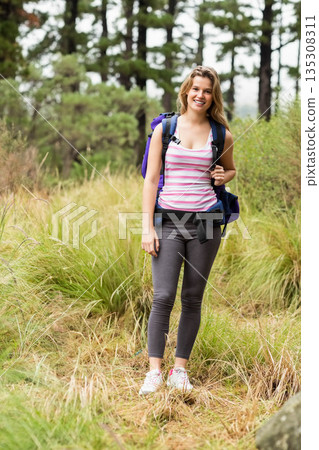 Female hiker standing on narrow pine forest trail wearing purple daypack and white sneakers Female hiker standing on narrow pine forest trail wearing purple daypack and white sneakers 135308311