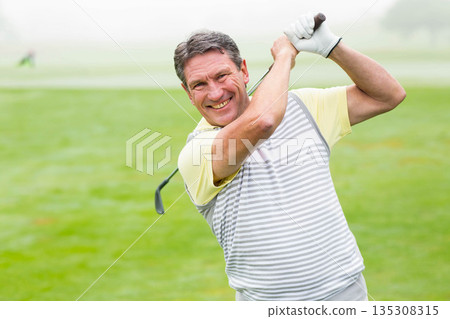 Senior African American man swinging golf club on fairway wearing striped polo shirt and glove Senior African American man swinging golf club on fairway wearing striped polo shirt and glove 135308315
