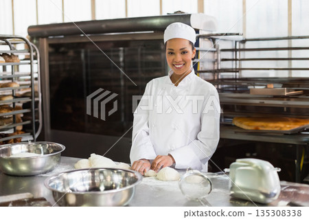 African American woman kneading dough on bakery prep table with stainless mixing bowls and sifter African American woman kneading dough on bakery prep table with stainless mixing bowls and sifter 135308338