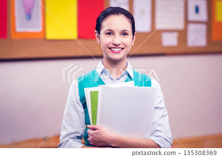 Female student in turquoise vest holding papers and notebooks before classroom bulletin board Female student in turquoise vest holding papers and notebooks before classroom bulletin board 135308369