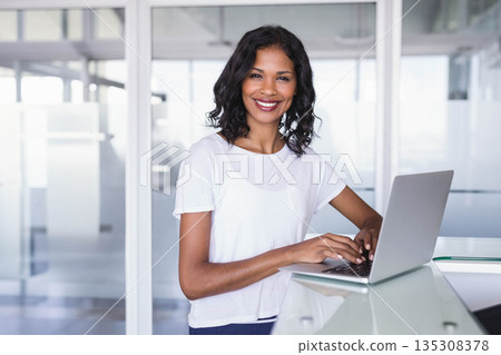 Female office worker using silver laptop on glossy white desk at reception with glass partitions 135308378