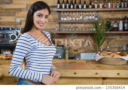 Woman barista leaning on wooden counter at cafe with espresso maker, pastry basket, copy space Woman barista leaning on wooden counter at cafe with espresso maker, pastry basket, copy space 135308414