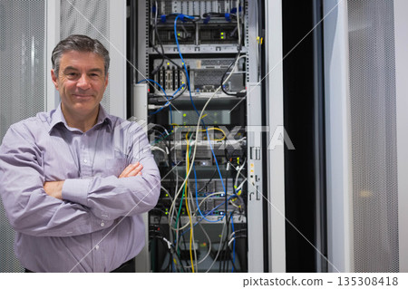 Male network technician monitoring server rack with colorful cables in data center, copy space 135308418