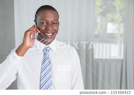 African American man in business attire talking on smartphone by sheer curtains in home workspace 135308422