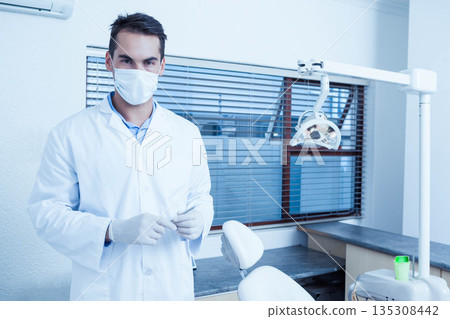 Male dentist wearing mask standing in clinic beside dental chair under overhead lamp, copy space Male dentist wearing mask standing in clinic beside dental chair under overhead lamp, copy space 135308442