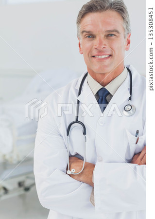Diverse coworkers wearing lab coats standing in clinical room near hospital bed with stethoscope Diverse coworkers wearing lab coats standing in clinical room near hospital bed with stethoscope 135308451