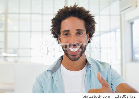Mid adult African American man standing in modern office by windows smiling and giving thumbs-up 135308452