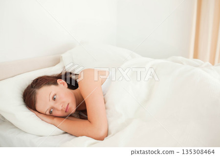 Woman lying on side wearing white tank top in bed with pillow and duvet, copy space 135308464