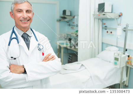 Senior male doctor standing with lab coat and stethoscope in hospital room, copy space 135308473