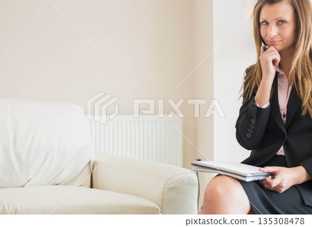 Woman in business attire thinking while holding pen and notebook on armchair at office, copy space 135308478