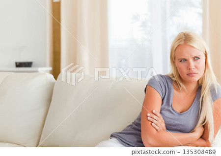Woman sitting on fabric sofa in living room, crossing arms and gazing toward window, copy space 135308489