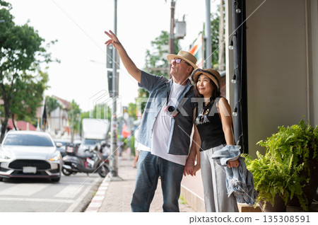 Old white man and asian woman holding hand walking on sidewalk touring around old town in Chiang mai Old white man and asian woman holding hand walking on sidewalk touring around old town in Chiang mai 135308591