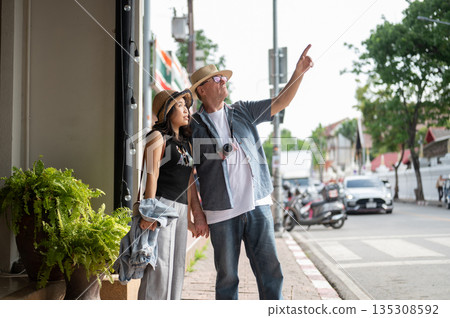 Old white man and asian woman holding hand walking on sidewalk touring old town street in Chiang mai Old white man and asian woman holding hand walking on sidewalk touring old town street in Chiang mai 135308592