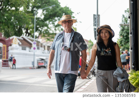 Old white man and asian woman holding hand walking on sidewalk along old town's street in Chiang mai Old white man and asian woman holding hand walking on sidewalk along old town's street in Chiang mai 135308593