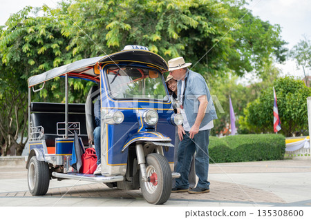 Old white man and wife talking to driver after riding in tuk tuk or three wheel taxi touring a city. 135308600