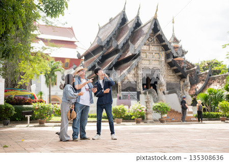 Old white man pointing with woman and Thai guide looking standing together in buddhist temple ground 135308636