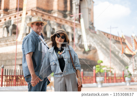Old white man and asian woman couple holding hand standing together in front of a pagoda in buddhist temple. 135308637