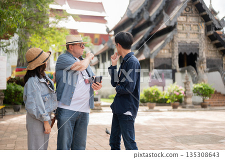 Old white man with phone talk or asking a guide with woman standing aside in buddhist temple grounds 135308643