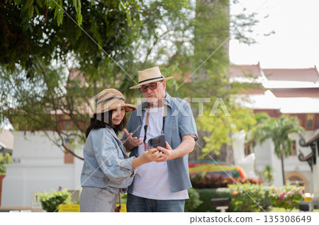 Old white man holding phone talking or asking asian woman while standing in a buddhist temple ground Old white man holding phone talking or asking asian woman while standing in a buddhist temple ground 135308649