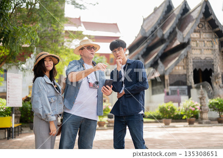 Old white man holding phone talk to asian guide with woman standing aside in buddhist temple grounds 135308651