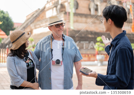 Old white man and asian woman listening to a guide standing aside ancient pagoda in buddhist temple. Old white man and asian woman listening to a guide standing aside ancient pagoda in buddhist temple. 135308659