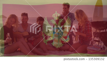 Sitting friends strumming acoustic guitar on beach at dusk, with bottles surfboard grill cooler bag 135309132