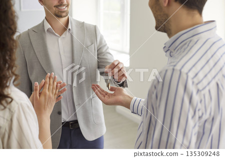 Real estate agent giving empty home apartment key to smiling homeowners Real estate agent giving empty home apartment key to smiling homeowners 135309248