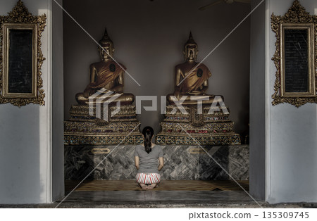 Young woman sitting praying pay respect to Buddha statue in the Wat Phra Chetuphon Wimon Mangkhalaram Ratchaworamahawihan. Worship pray. Young woman sitting praying pay respect to Buddha statue in the Wat Phra Chetuphon Wimon Mangkhalaram Ratchaworamahawihan. Worship pray. 135309745