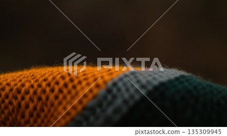 Textured fabric showcasing a vibrant pattern of orange, green, and gray threads in a warm setting Textured fabric showcasing a vibrant pattern of orange, green, and gray threads in a warm setting 135309945