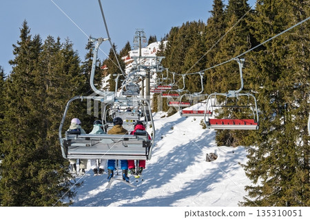 Skiers Ascending Mountain on Chairlift Winter Adventure in Snowy Alpine Landscape Skiers Ascending Mountain on Chairlift Winter Adventure in Snowy Alpine Landscape 135310051