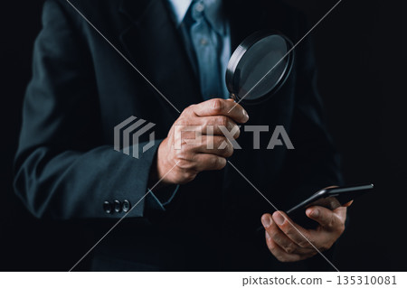 businessman holds smartphone and inspects it closely using a magnifying glass, symbolizing investigation, digital scrutiny, cybersecurity analysis, search engine or detailed mobile data examination. businessman holds smartphone and inspects it closely using a magnifying glass, symbolizing investigation, digital scrutiny, cybersecurity analysis, search engine or detailed mobile data examination. 135310081