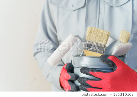 A person in work clothes holding a bucket filled with brushes and rollers | Renovation, painting contractor, DIY image A person in work clothes holding a bucket filled with brushes and rollers | Renovation, painting contractor, DIY image 135310102