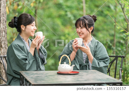 A young Asian woman in a yukata drinking tea while taking a forest bath on a trip 135310157
