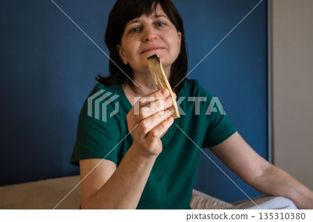 Woman holding smoldering palo santo stick, practicing spiritual cleansing and aromatherapy 135310380