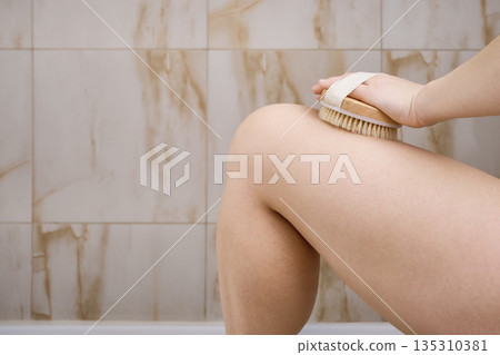 Woman dry brushing her leg, promoting skin blood circulation and exfoliation for wellness 135310381