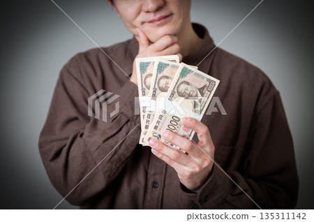 一位身著休閒裝的中年男商人正為一沓現金憂心忡忡。 一位身著休閒裝的中年男商人正為一沓現金憂心忡忡。 135311142