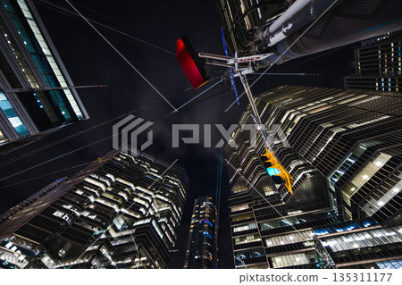 Glass towers rise sharply into the night as cables stretch overhead like the strings of a giant urban instrument 135311177