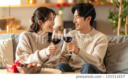 一對笑容滿面的日本年輕夫婦在客廳裡一邊喝著葡萄酒一邊慶祝他們的結婚紀念日。 135311657