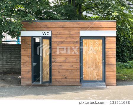 Wooden public restroom building surrounded by trees. Wooden public restroom building surrounded by trees. 135311688