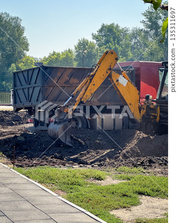 Excavator digging at a construction site with a truck nearby. Excavator digging at a construction site with a truck nearby. 135311697
