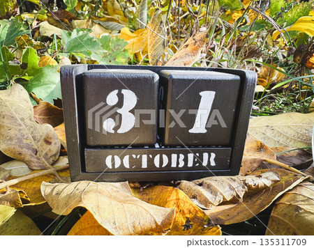 Wooden calendar displaying October 31 among autumn leaves. 135311709