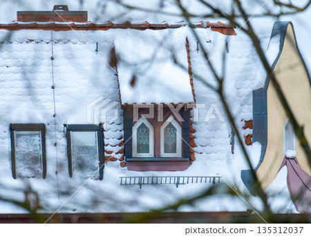 A view of a tiled roof covered in a thick layer of fluffy snow. Traditional architecture, dormers, and a wintry atmosphere in the city. A view of a tiled roof covered in a thick layer of fluffy snow. Traditional architecture, dormers, and a wintry atmosphere in the city. 135312037